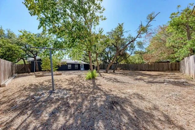 a view of a backyard with large trees and wooden fence