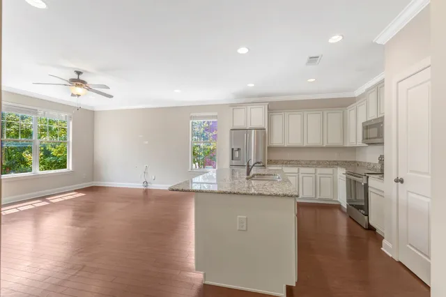 a kitchen with stainless steel appliances granite countertop a sink a stove a refrigerator and white cabinets with wooden floor