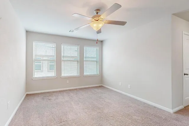 an empty room with chandelier fan and windows