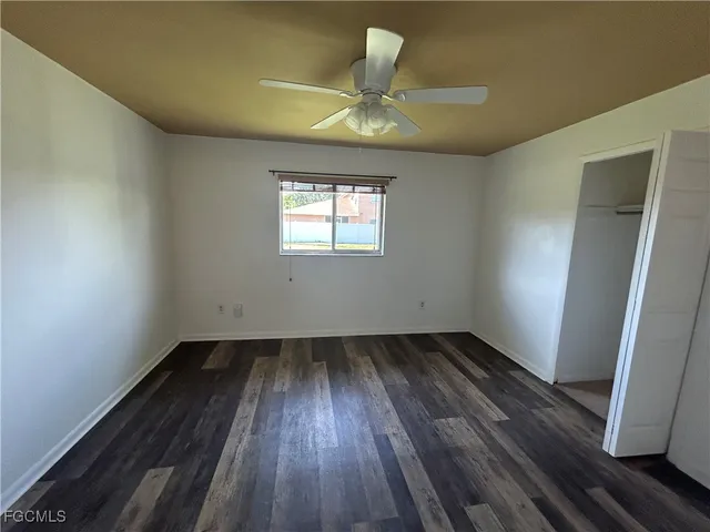 an empty room with wooden floor chandelier fan and windows