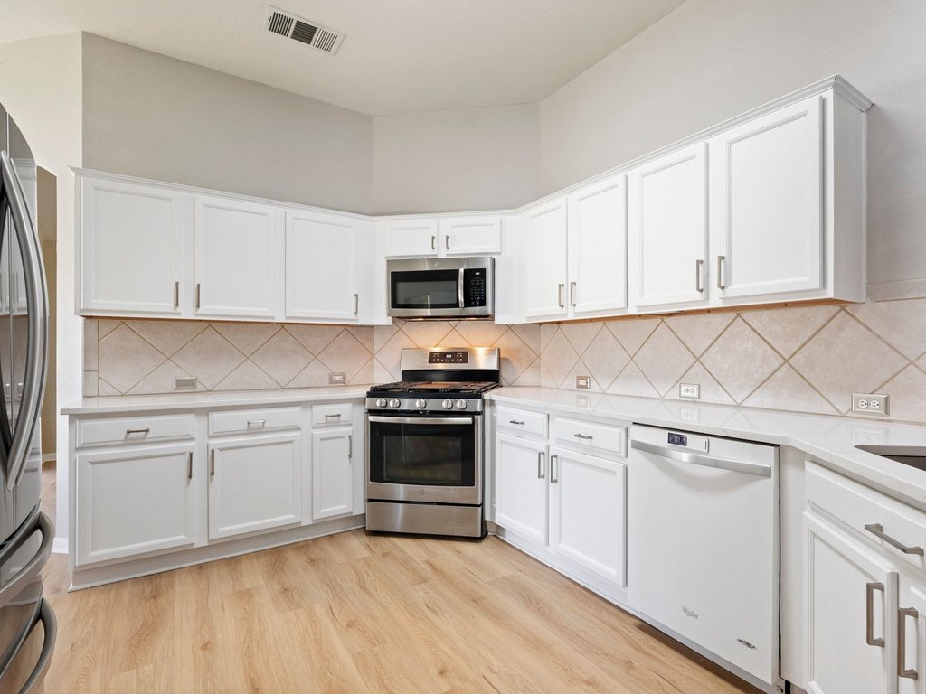 1201 Ridgewood Drive Leander, TX 78641 - Photo 5 of 29 Kitchen featuring white cabinets, stainless steel appliances, light wood-style floors, light stone countertops, and decorative backsplash