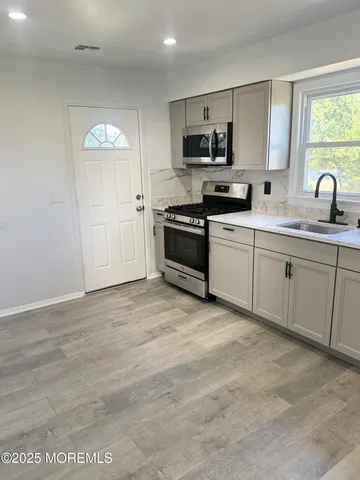 a large kitchen with stainless steel appliances granite countertop a stove a sink dishwasher and a microwave oven with white cabinets