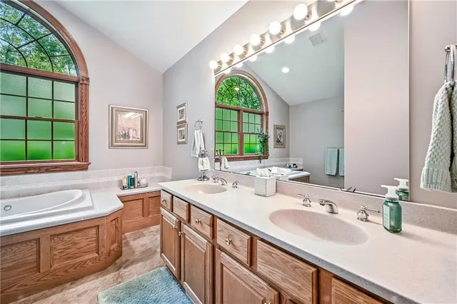 a bathroom with a double vanity sink a mirror and a bathtub next to a window