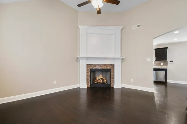 a view of a livingroom with a fireplace a ceiling fan and wooden floor
