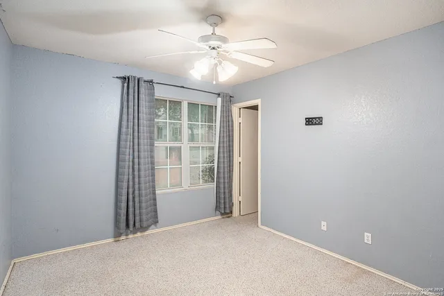 an empty room with chandelier fan and windows