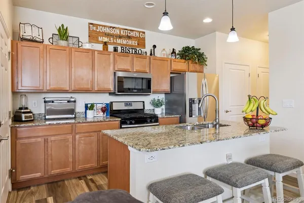a kitchen with stainless steel appliances granite countertop a sink a stove a microwave a refrigerator cabinets and chairs