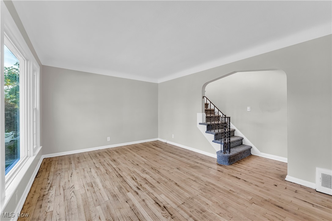 Unfurnished living room featuring stairs, light wood-style flooring, and arched walkways