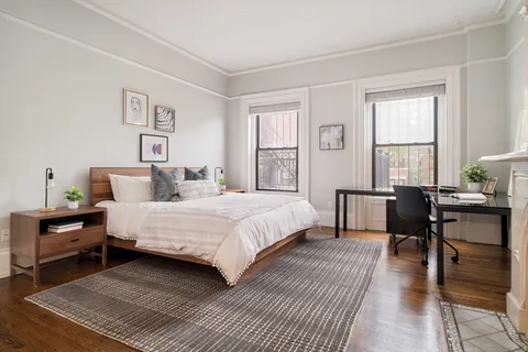 a bedroom with a bed a table and chair with wooden floor