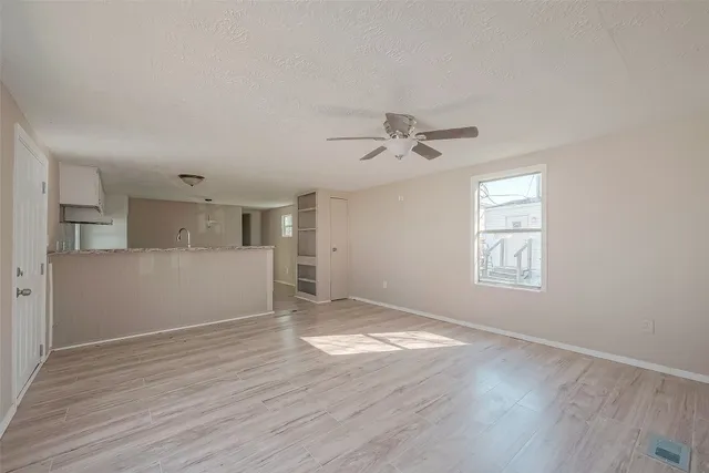 an empty room with wooden floor chandelier fan and windows