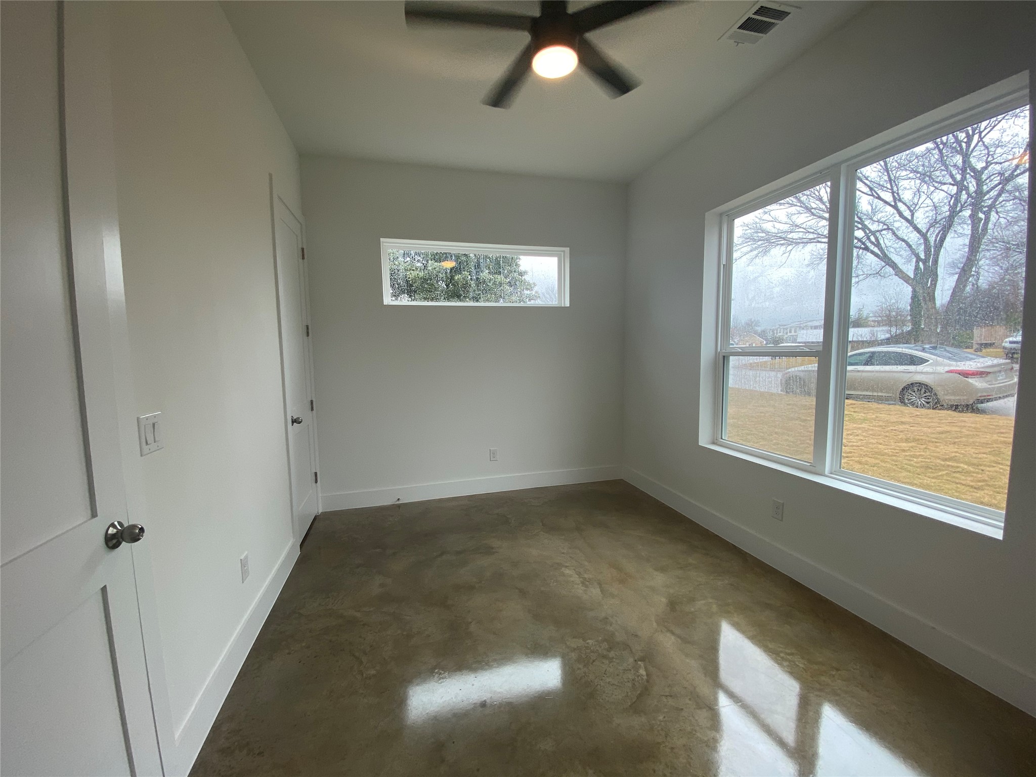 1916 Webberville Road, Unit B Austin, TX 78721 - Photo 11 of 25 Interior room featuring sleek concrete flooring, a modern ceiling fan with integrated lighting, and multiple windows providing ample natural illumination