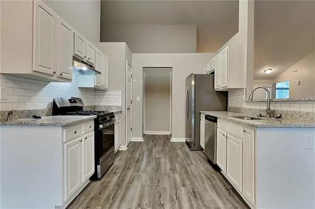 a kitchen with stainless steel appliances granite countertop a refrigerator a sink dishwasher a stove and white countertops with wooden floor