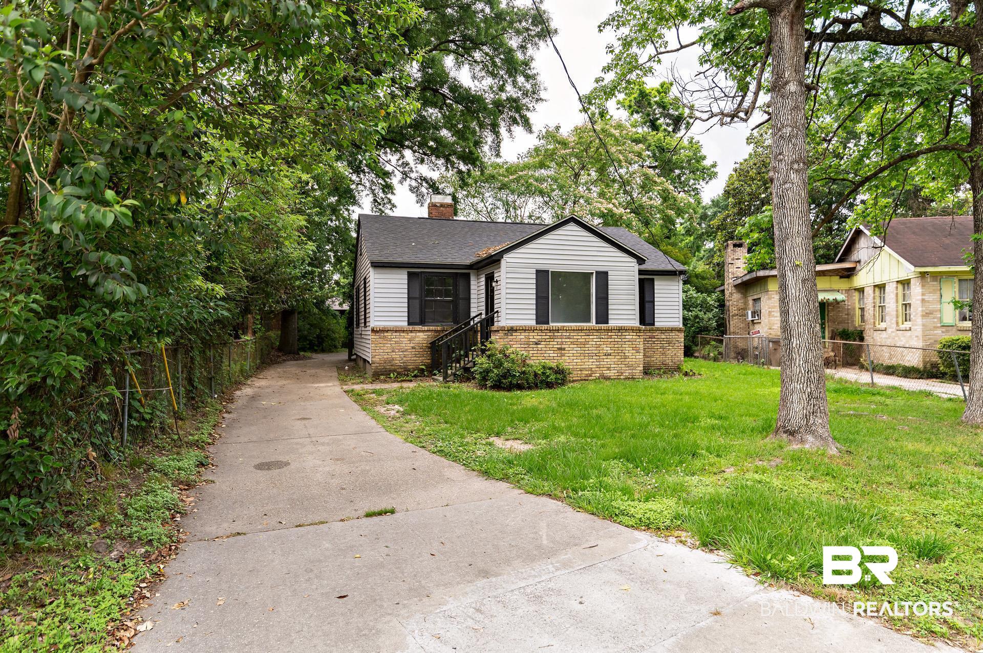 1869 Mott Drive West Mobile, AL 36617 - Photo 1 of 34 Bungalow-style home with concrete driveway, a chimney, fence, brick siding, and a front lawn