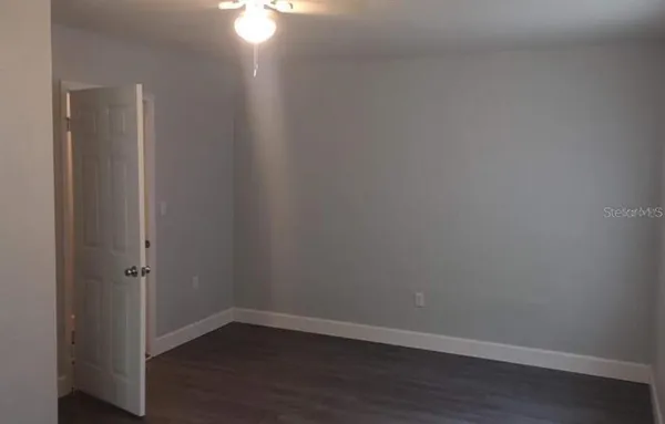 a view of an empty room with wooden floor and a fan