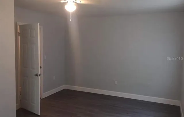 a view of an empty room with wooden floor and a fan