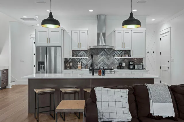 a kitchen with stainless steel appliances a refrigerator a sink a stove a dining table and chairs with wooden floor