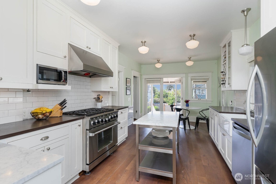 1607 6th Avenue West Seattle, WA 98119 - Photo 8 of 27 a kitchen with stainless steel appliances a stove a sink dishwasher a refrigerator white cabinets and wooden floor