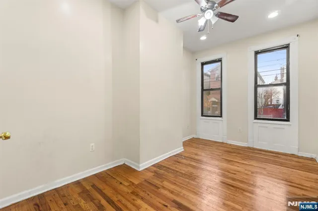 an empty room with wooden floor chandelier fan and windows