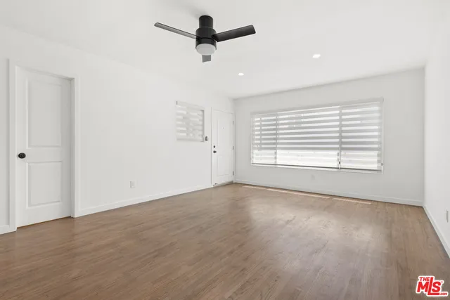 an empty room with wooden floor ceiling fan and windows