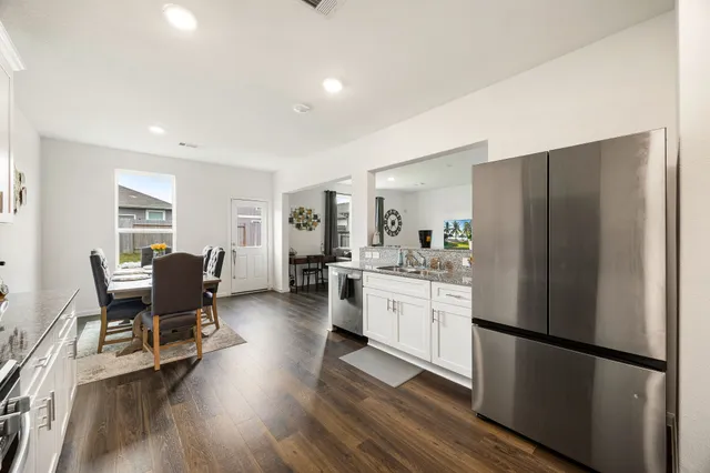 a kitchen with stainless steel appliances granite countertop a refrigerator a stove a sink dishwasher a dining table and chairs with wooden floor