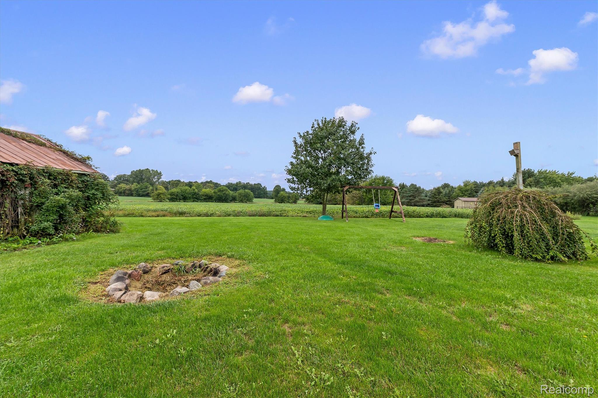 3553 North State Road Owosso, MI 48867 - Photo 38 of 45 Expansive green lawn with a stone-lined fire pit, mature trees, and landscaping