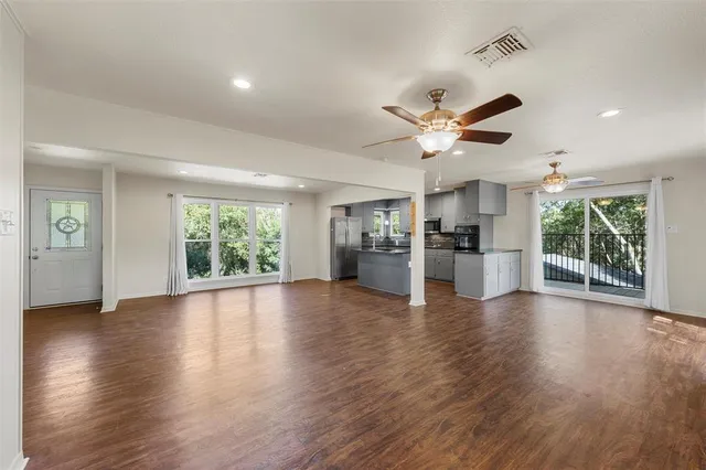a view of an empty room with wooden floor and a kitchen