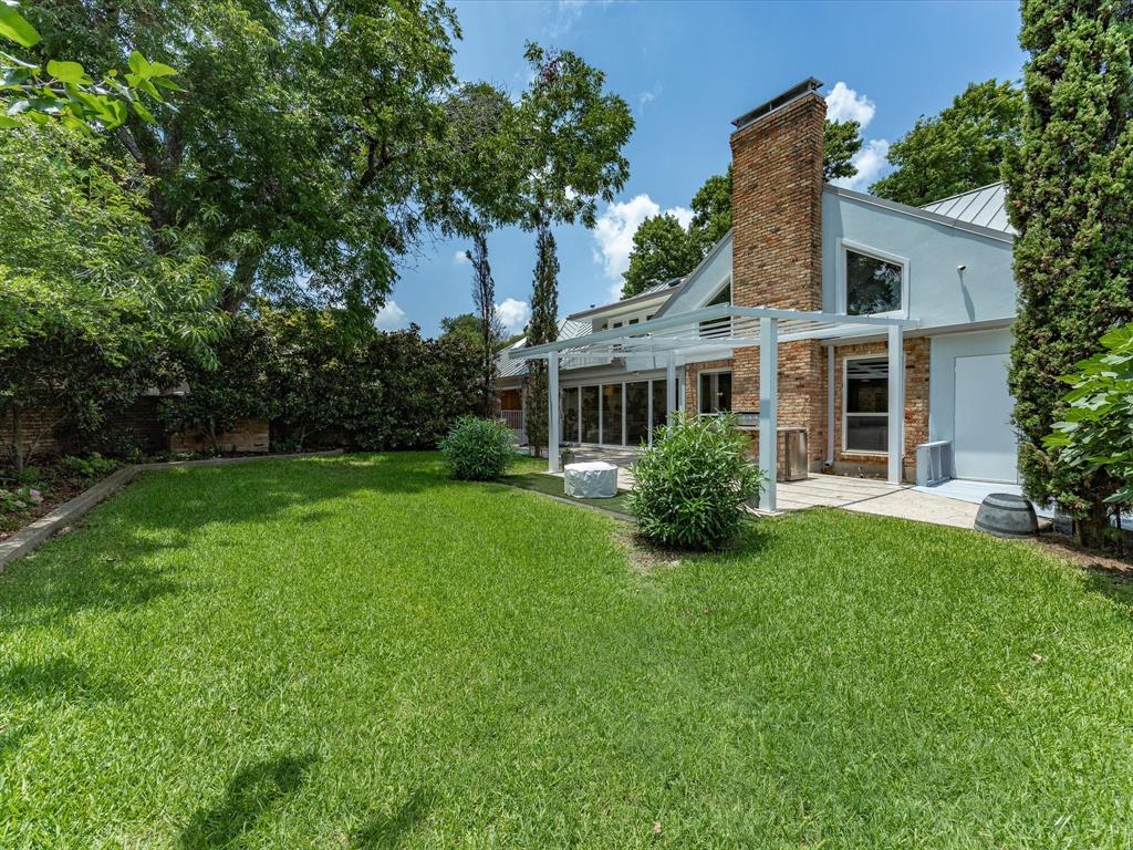 6160 Spring Valley Road Dallas, TX 75240 - Photo 36 of 40 Expansive green lawn with a spacious outdoor deck, featuring a light-colored metal roof and a brick chimney