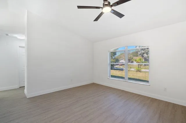 an empty room with wooden floor fan and windows