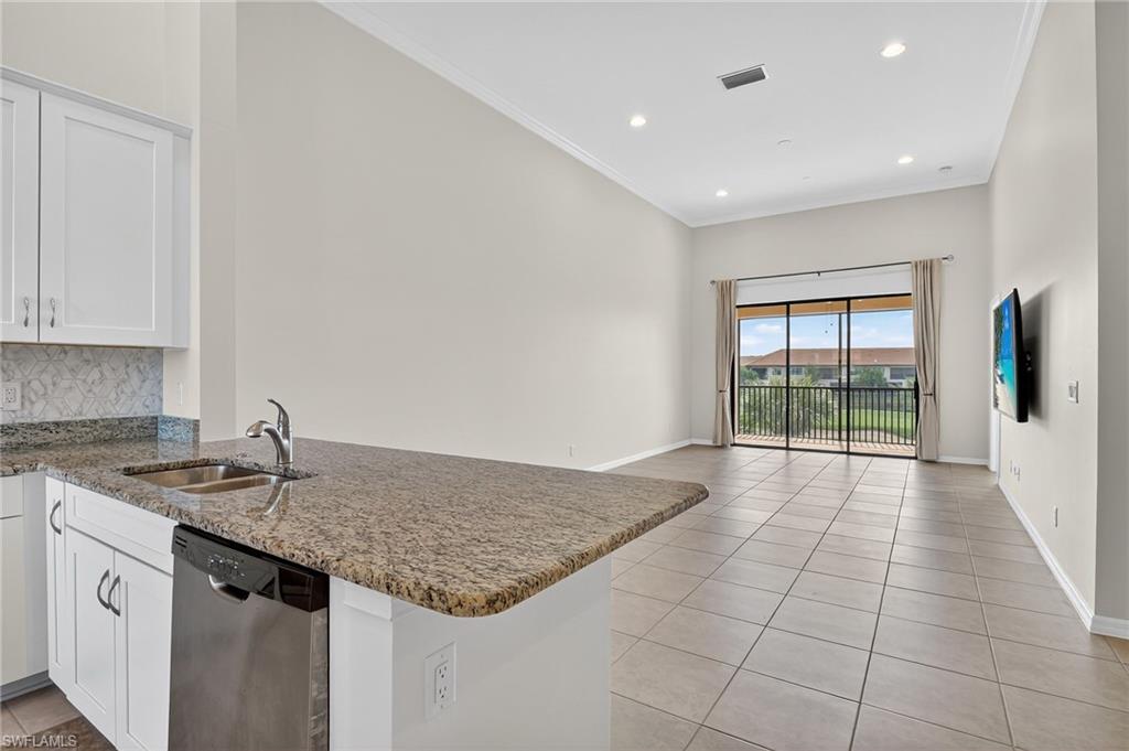 9386 Pocida Court, Unit 202 Naples, FL 34119 - Photo 12 of 38 Kitchen featuring stainless steel dishwasher, a peninsula, light tile patterned flooring, white cabinetry, and stone countertops