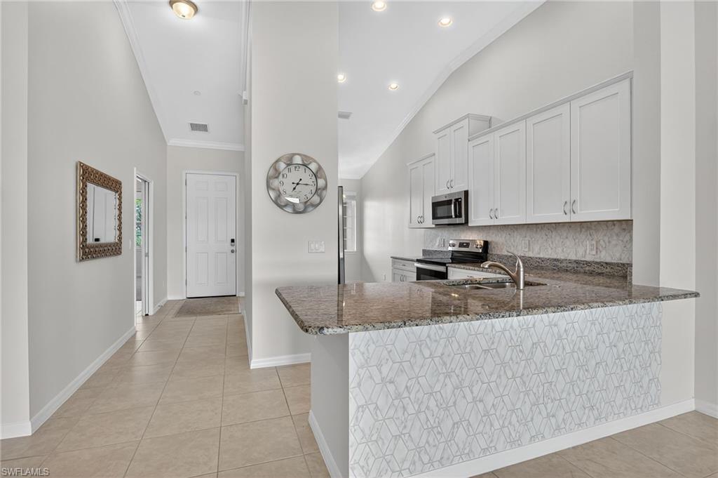 9386 Pocida Court, Unit 202 Naples, FL 34119 - Photo 14 of 38 Kitchen with dark stone countertops, vaulted ceiling, appliances with stainless steel finishes, light tile patterned floors, and tasteful backsplash