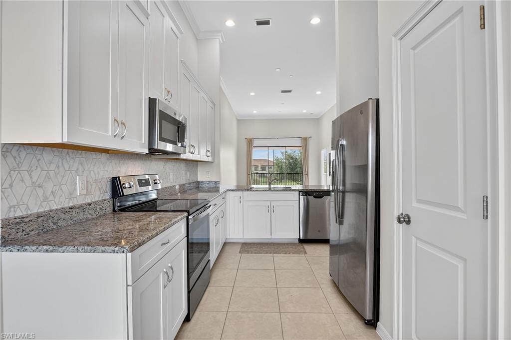 9386 Pocida Court, Unit 202 Naples, FL 34119 - Photo 9 of 38 Kitchen featuring appliances with stainless steel finishes, white cabinets, light tile patterned floors, tasteful backsplash, and dark stone counters