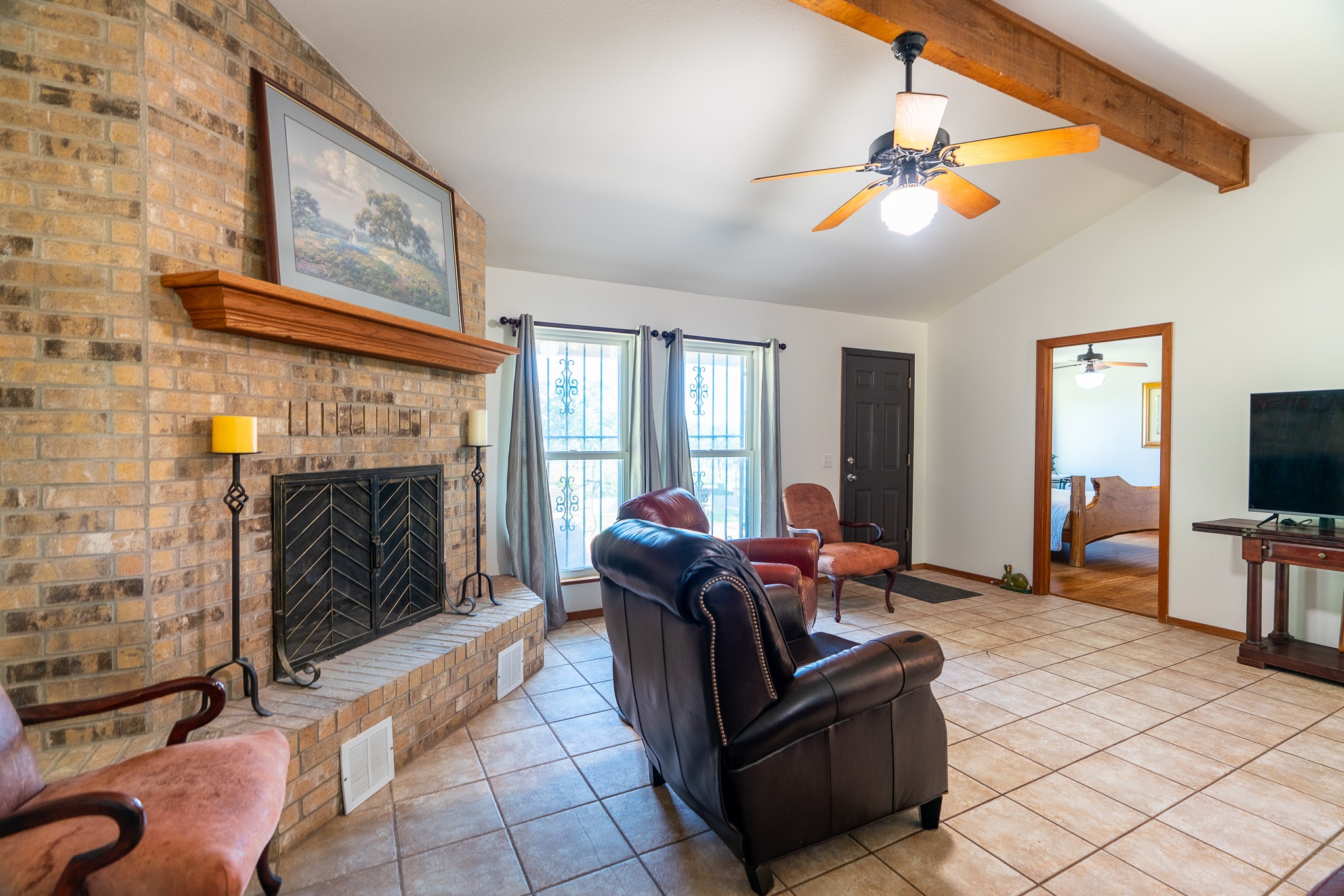 400 619th Spur Elgin, TX 78621 - Photo 24 of 40 A cozy living space features a prominent brick fireplace with a mantle, complemented by tiled flooring and exposed ceiling beams.