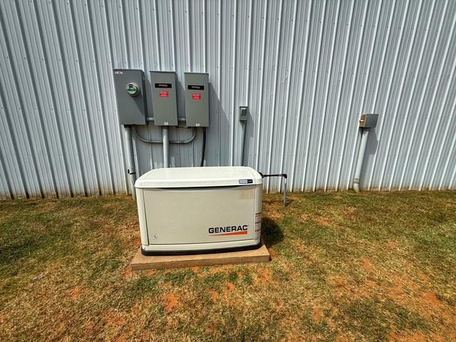 36469 1330th Road Wewoka, OK 74884 - Photo 19 of 39 Generac generator unit on a concrete pad, electrical conduit with multiple service boxes, and a corrugated metal wall