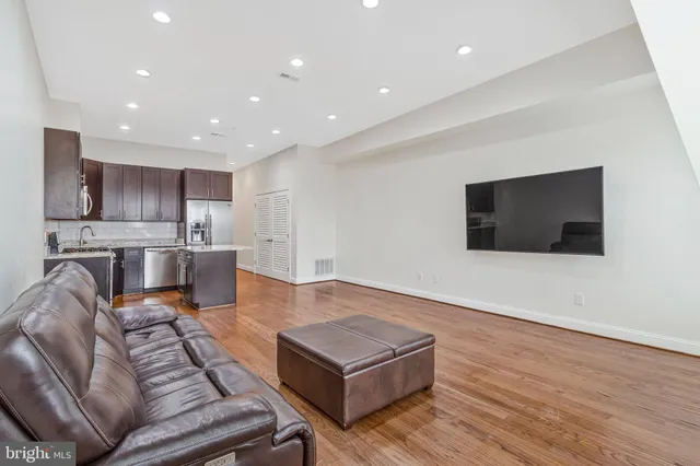 a living room with stainless steel appliances furniture a flat screen tv and a kitchen view