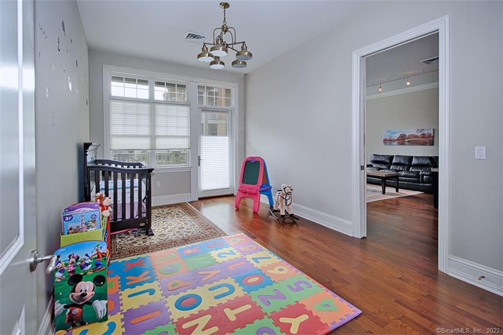 100 Stone Ridge Way, Unit 1H Fairfield, CT 06824 - Photo 22 of 30 a playing room with a baby crib and a wooden floor