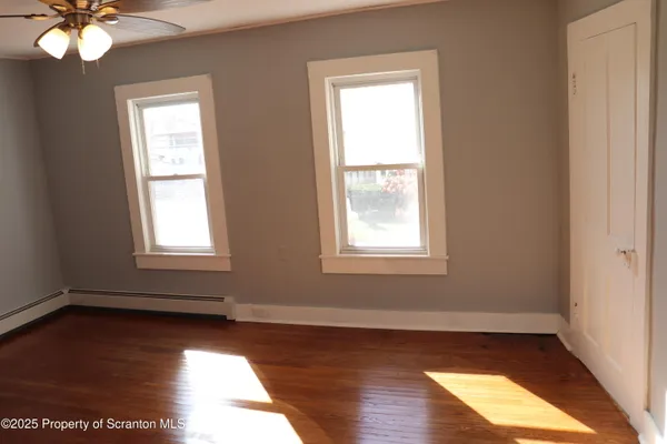 an empty room with wooden floor fan and windows
