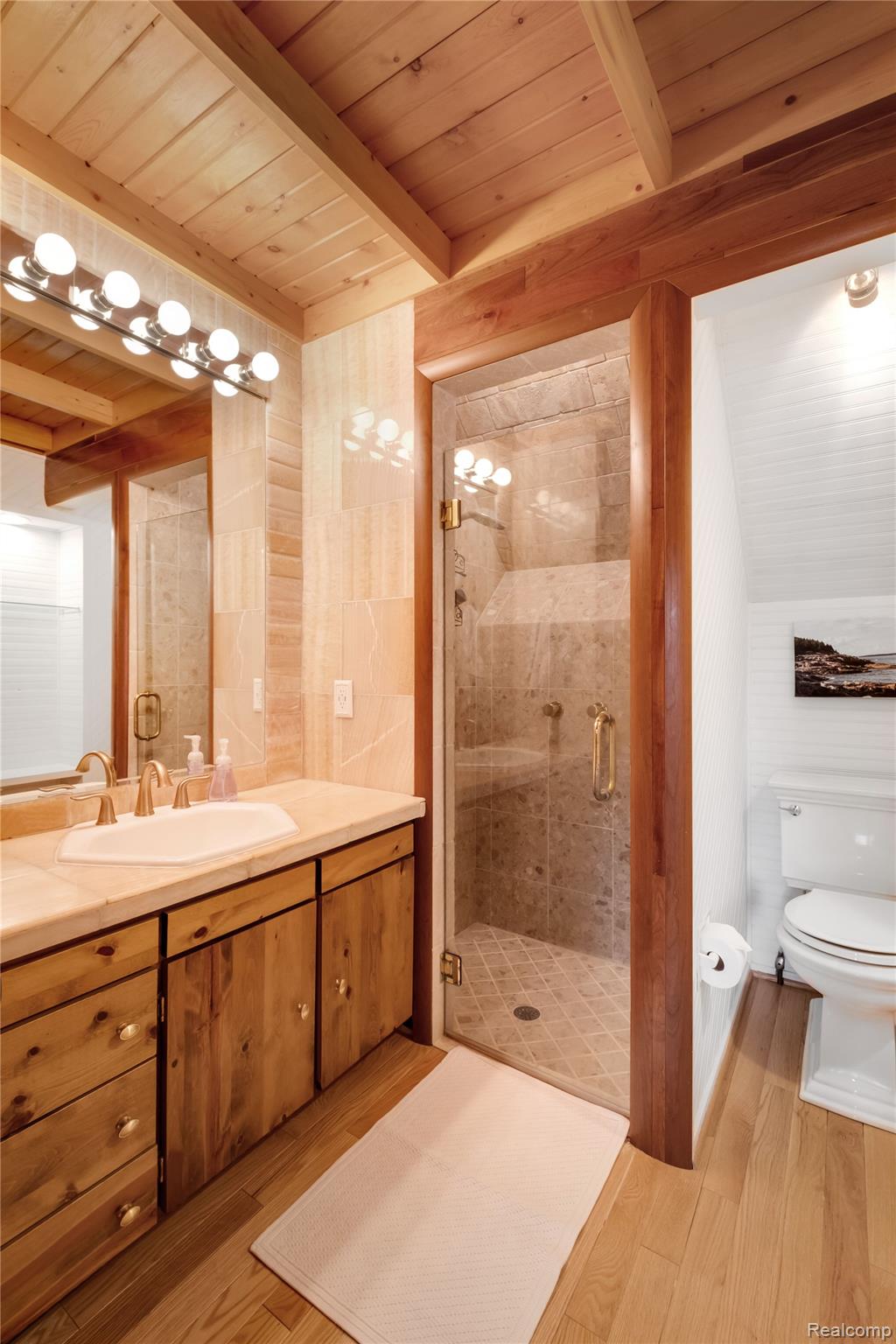 15420 Jennings Road Fenton, MI 48430 - Photo 20 of 45 Wood-finish plank flooring, wood-beamed ceiling, wood-finish vanity with countertop, glass-enclosed shower with tile surround, and an octagonal sink basin