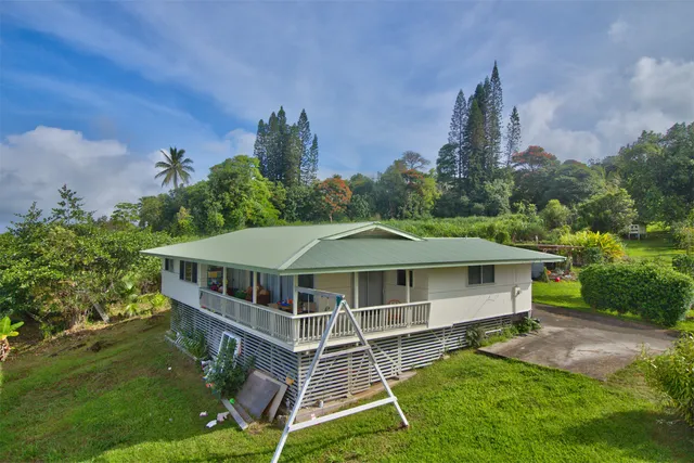 a white house with a big yard plants and large trees