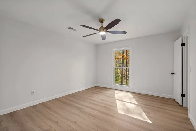 an empty room with wooden floor ceiling fan and windows