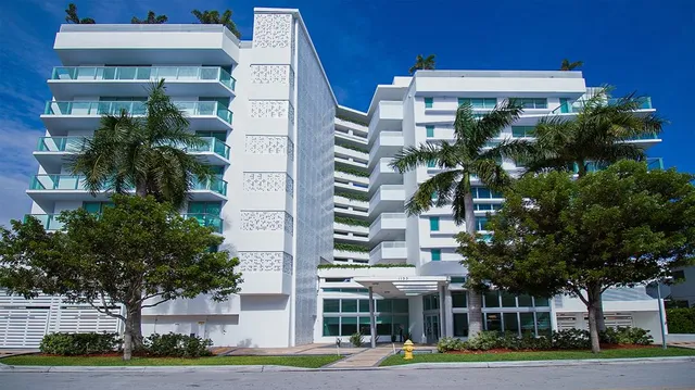 a front view of a multi story residential apartment building with yard and parking space