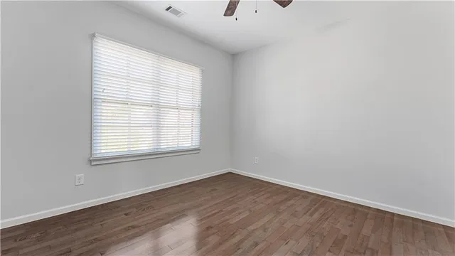 an empty room with wooden floor chandelier fan and windows