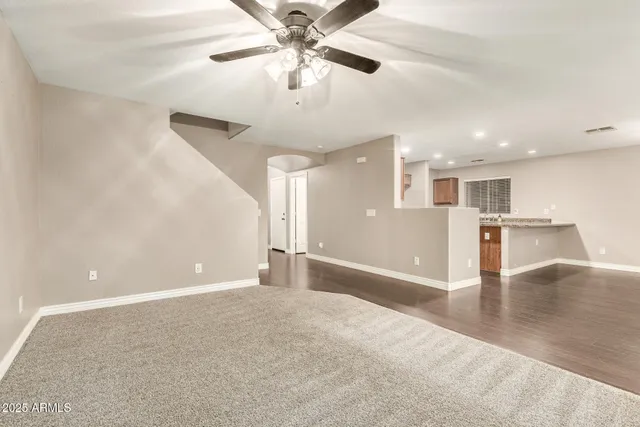 a view of an empty room with kitchen view and a ceiling fan