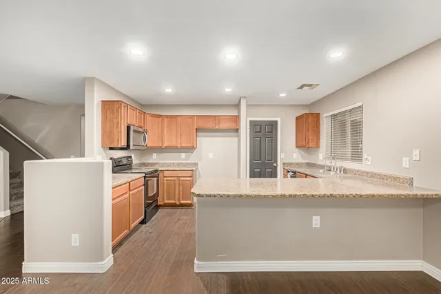 a large kitchen with kitchen island a stove a sink a refrigerator wooden floor and cabinets