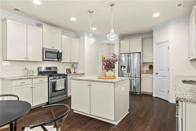 a kitchen with stainless steel appliances granite countertop a stove a sink a refrigerator and a dining table with wooden floor