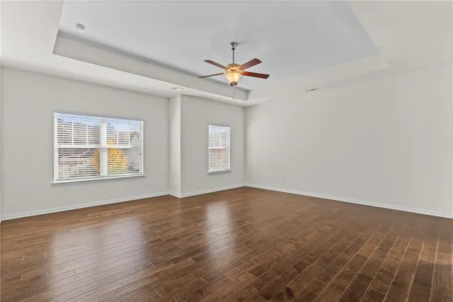 an empty room with wooden floor ceiling fan and windows