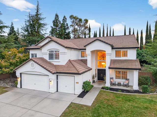 a view of a white house with a small yard and large trees