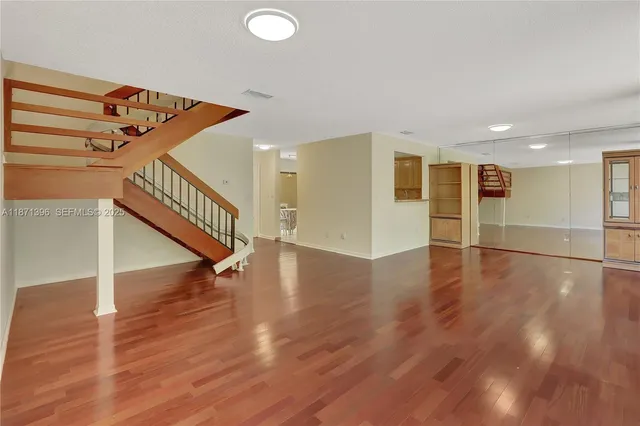 a view of an empty room with wooden floor and stairs