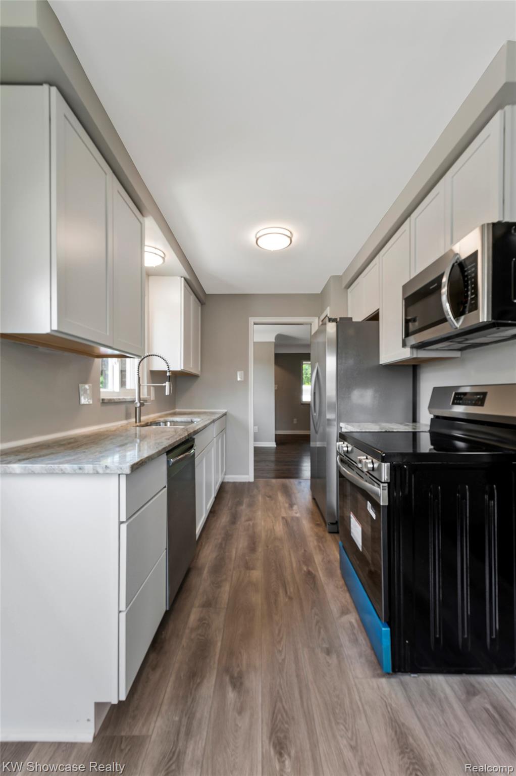 8936 Merriman Road Livonia, MI 48150 - Photo 26 of 49 Galley kitchen featuring wood-finish flooring, white cabinetry, integrated stainless steel appliances, and light-toned countertops