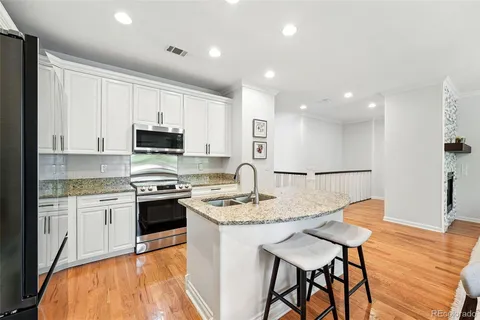 a large kitchen with stainless steel appliances granite countertop a stove a sink a refrigerator and white cabinets with wooden floor