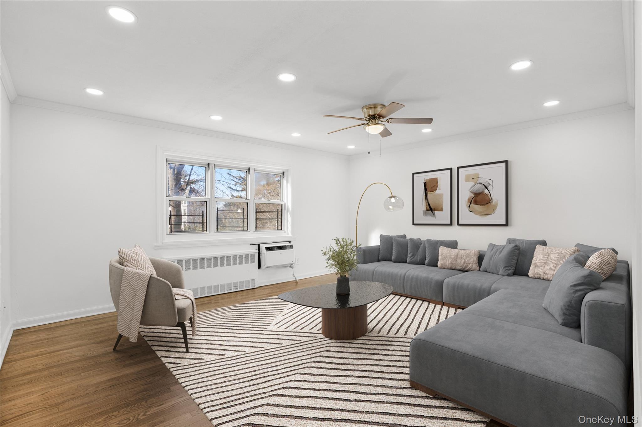 Welcome home! Virtually staged living room with ornamental molding, radiator heating unit, recessed lighting, wood finished floors, and a ceiling fan