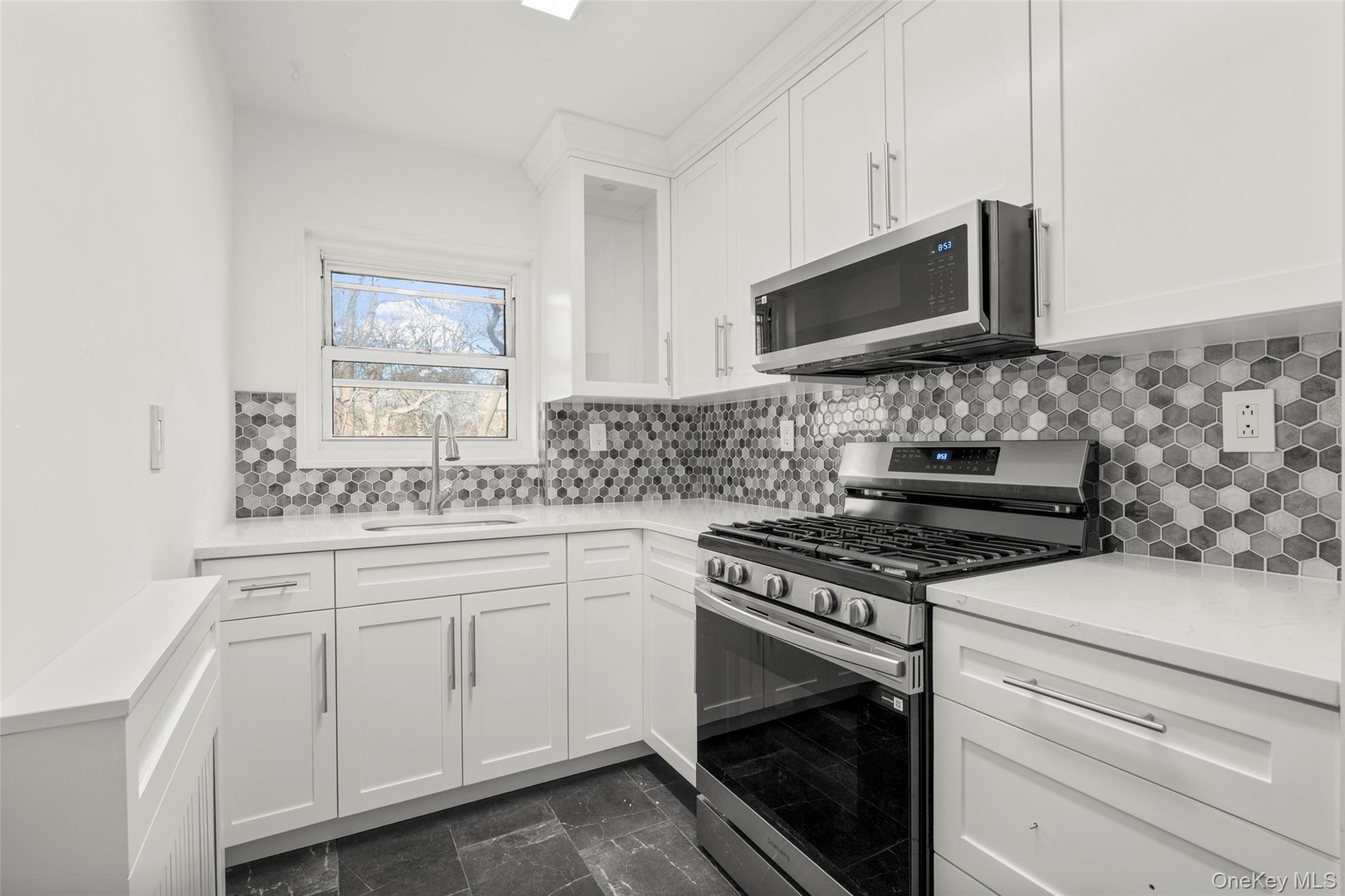 179 Drake Avenue, Unit 2J New Rochelle, NY 10805 - Photo 5 of 16 Kitchen with stainless steel appliances, white cabinetry, dark marble finish flooring, tasteful backsplash, and light stone counters
